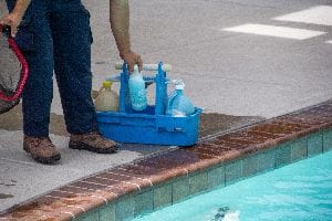 Pool Cleaner Standing Next To An Inground Pool With Supplies